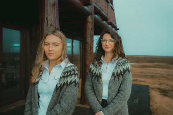 Two girls wear grey lopapeysa sweaters and white collared shirts outside the Hotel Rangá Restaurant in south Iceland.