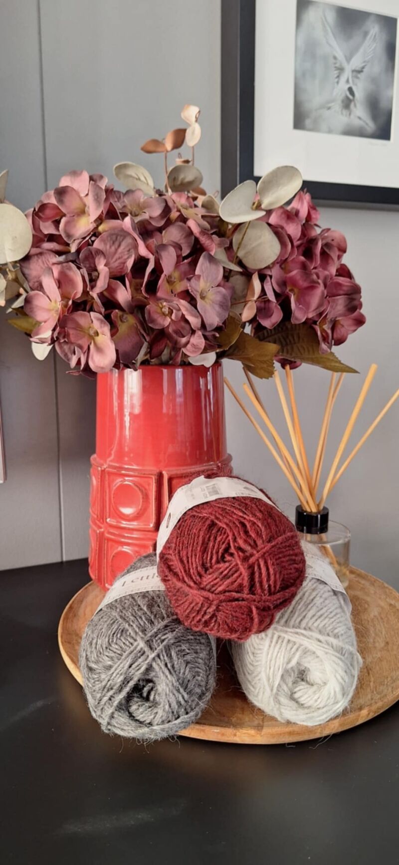 A photo of three skeins of yarn in varying shades beside a vase filled with purple flowers.