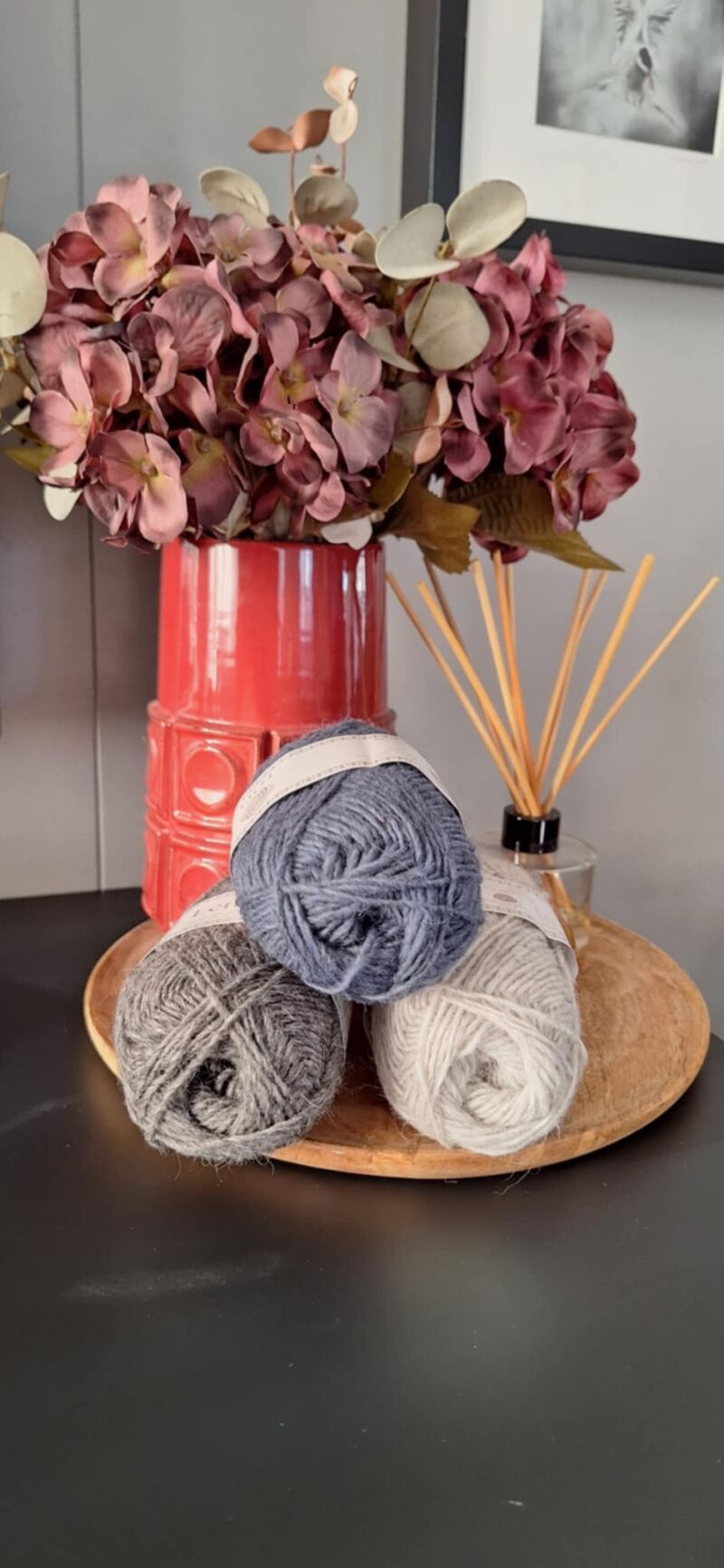 A photo of three skeins of yarn in varying shades beside a vase filled with purple flowers.