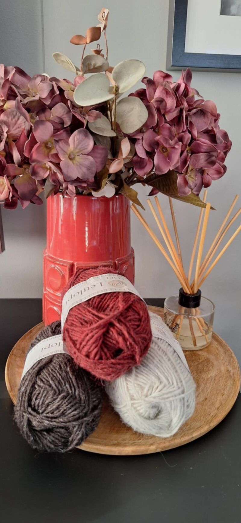 A photo of three skeins of yarn in varying shades beside a vase filled with purple flowers.