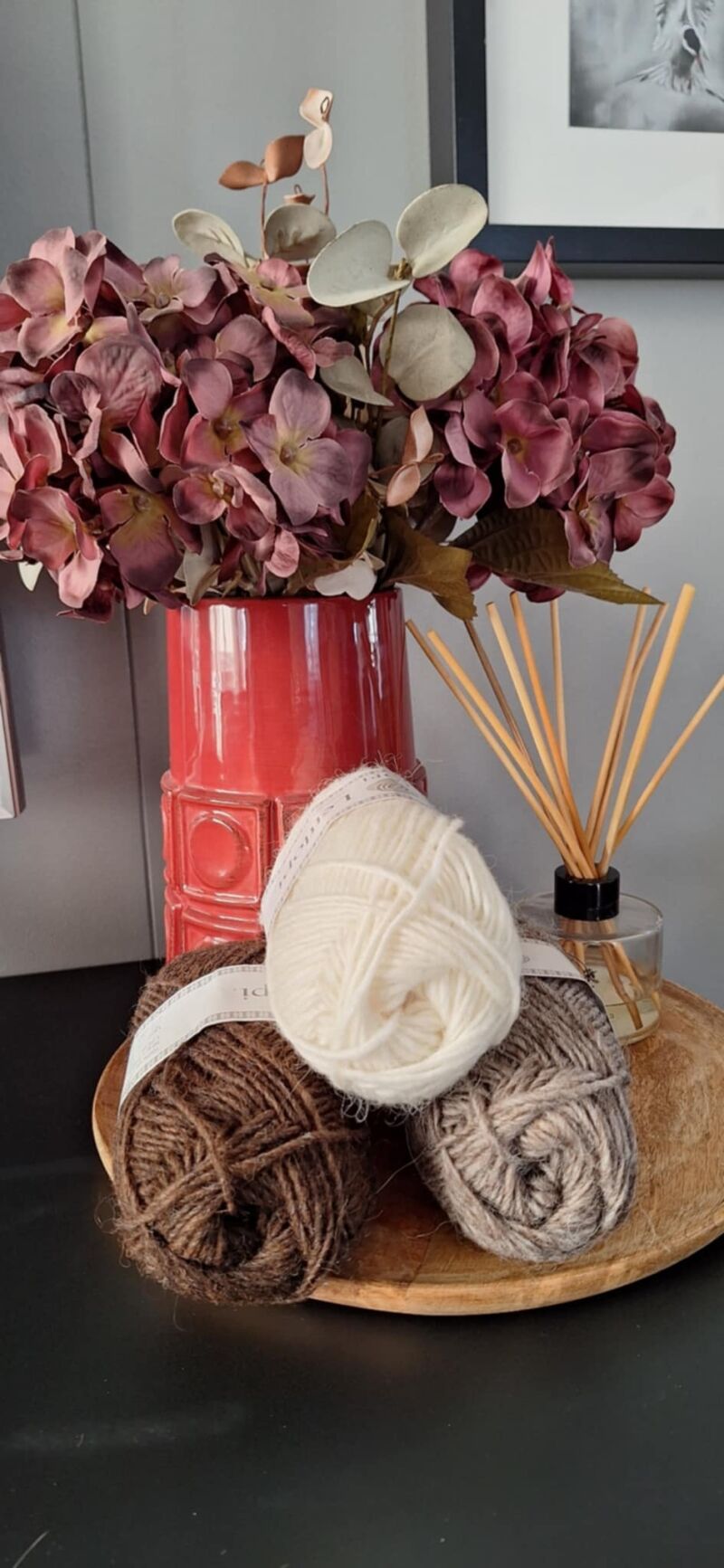 A photo of three skeins of yarn in varying shades beside a vase filled with purple flowers.